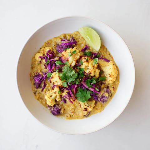 Steaming bowl of Red Cabbage, Cauliflower & Coconut Dhal, garnished with fresh cilantro and lime wedges.