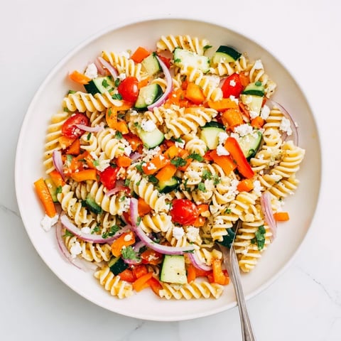 Pasta salad with seasonal veggies showcasing bright colors and a light, flavorful dressing.