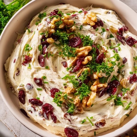 Creamy lightened holiday cream cheese dip with vibrant red cranberries and fresh green herbs in a bowl.