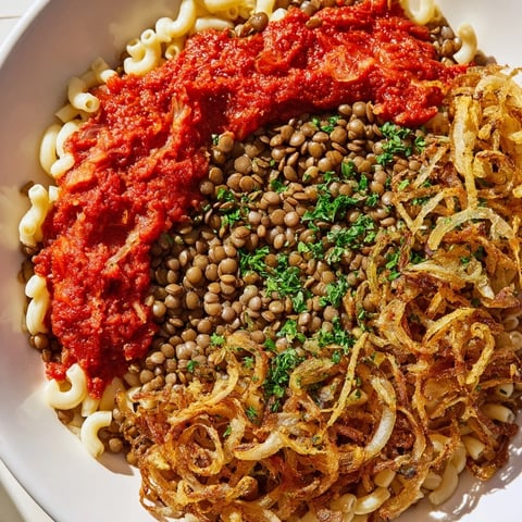 Steaming Egyptian Koshari: a vibrant, layered dish featuring a rich tomato sauce and crispy onions.