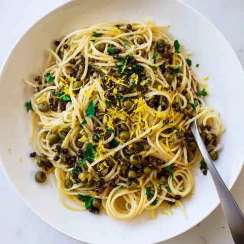 A close-up of Olive Tapenade Pasta twirled on a fork, with chopped parsley and lemon zest garnish.
