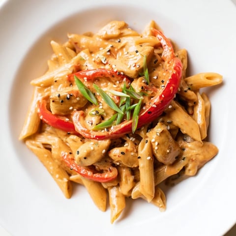 Golden, tender chicken pieces and glossy penne pasta coated in a creamy, vibrant sweet chili sauce, garnished with fresh green onions.  