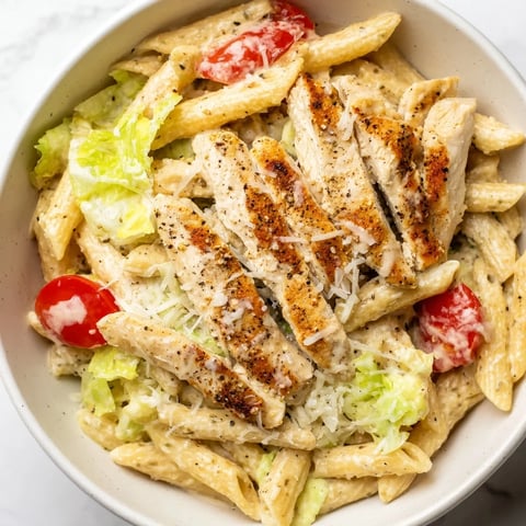 A vibrant bowl of Spicy Chicken Caesar Pasta topped with grilled chicken, crisp romaine, and shaved Parmesan cheese.