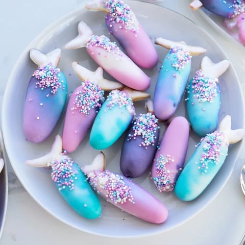 A close-up of Mignardises Queue de Sirène showcases airy madeleines coated in white chocolate and mermaid sprinkles.