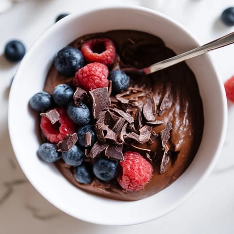 Creamy Avocado Chocolate Pudding, a vegan delight, is pictured alongside shaved dark chocolate.