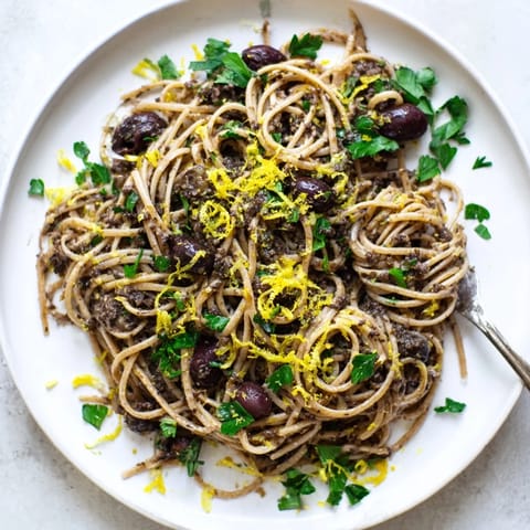 A rustic skillet of Olive Tapenade Pasta, featuring Kalamata olives and capers, served warm with a side salad.