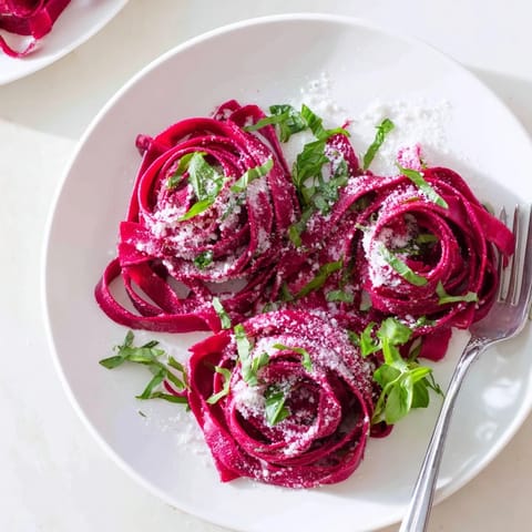 Vibrant magenta beet noodles resting on a marble surface, ready to be served with Parmesan cheese.  