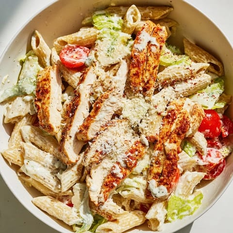 Spicy Chicken Caesar Pasta in a white bowl features al dente penne tossed with creamy dressing and bright cherry tomatoes.