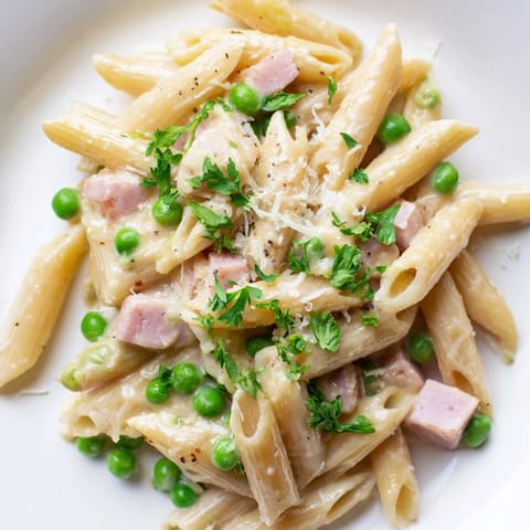 Spring Pea & Ham Pasta steaming in a skillet, garnished with chopped parsley and a sprinkle of extra cheese.