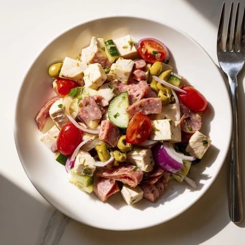 The Italian Deli Chopped Chicken Salad is served in a rustic wooden bowl, drizzled with a vibrant green herb-packed dressing and garnished with sliced pepperoncini.  