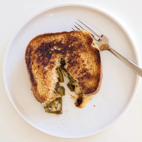 A close-up view of a Jalapeño Pepper Jack Grilled Cheese sandwich cut in half, revealing creamy melted filling.