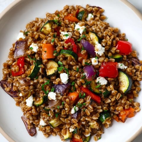 Hearty Mediterranean farro bowl with caramelized veggies, topped with crumbled feta and a drizzle of balsamic dressing.  