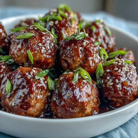Tender Easy Sweet and Sour Crock Pot Meatballs garnished with green onions and sesame seeds, served as a party appetizer.