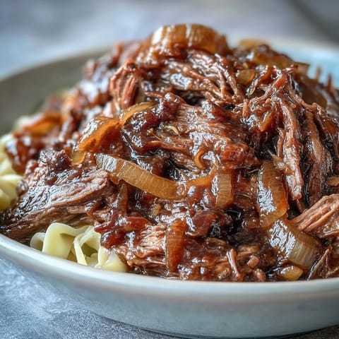 Shredded beef and caramelized onion gravy coat buttery egg noodles, garnished with fresh parsley.