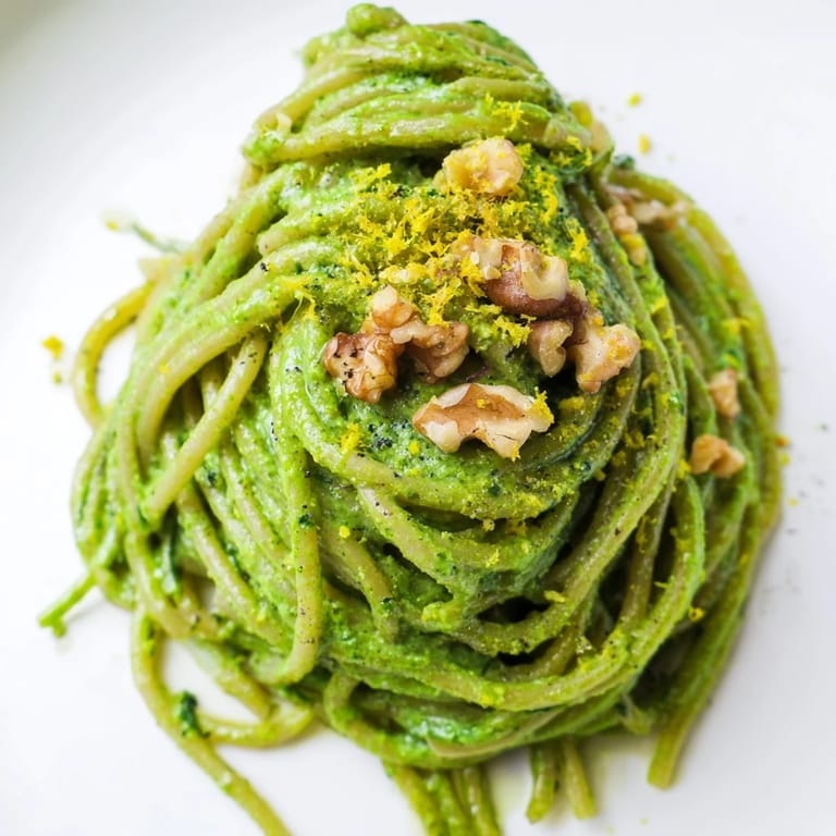 A bowl of creamy spinach walnut pasta garnished with chopped walnuts, lemon zest, and cracked black pepper, ready to serve.  