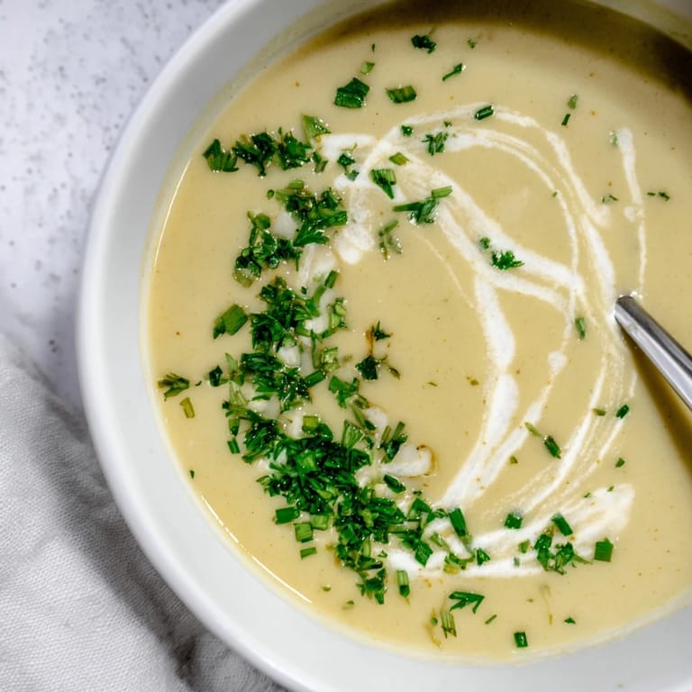Roasted parsnip and herb soup served with a side of crusty bread on a wooden table.
