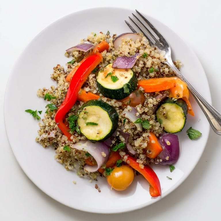 Colorful quinoa vegetable pilaf with roasted bell peppers and zucchini, topped with parsley and mint for a fresh finish.