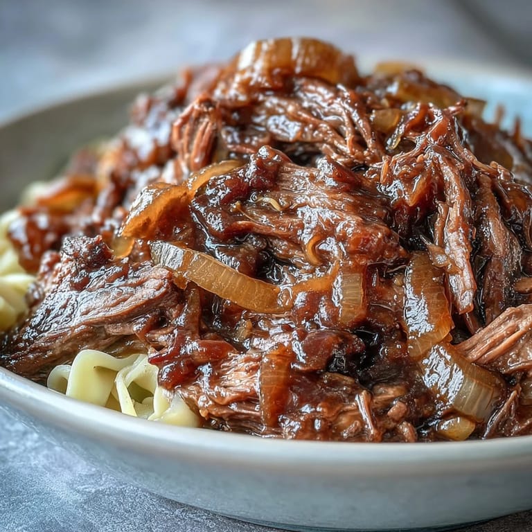 Shredded beef and caramelized onion gravy coat buttery egg noodles, garnished with fresh parsley.
