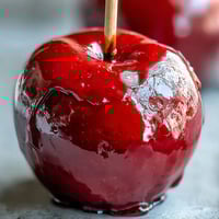 Bright red candy apples with glossy shells and wooden sticks, perfect for festive fall gatherings.