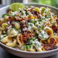 Creamy elote pasta salad with cotija, chili, and lime, featuring charred corn and zesty dressing in a vibrant bowl.
